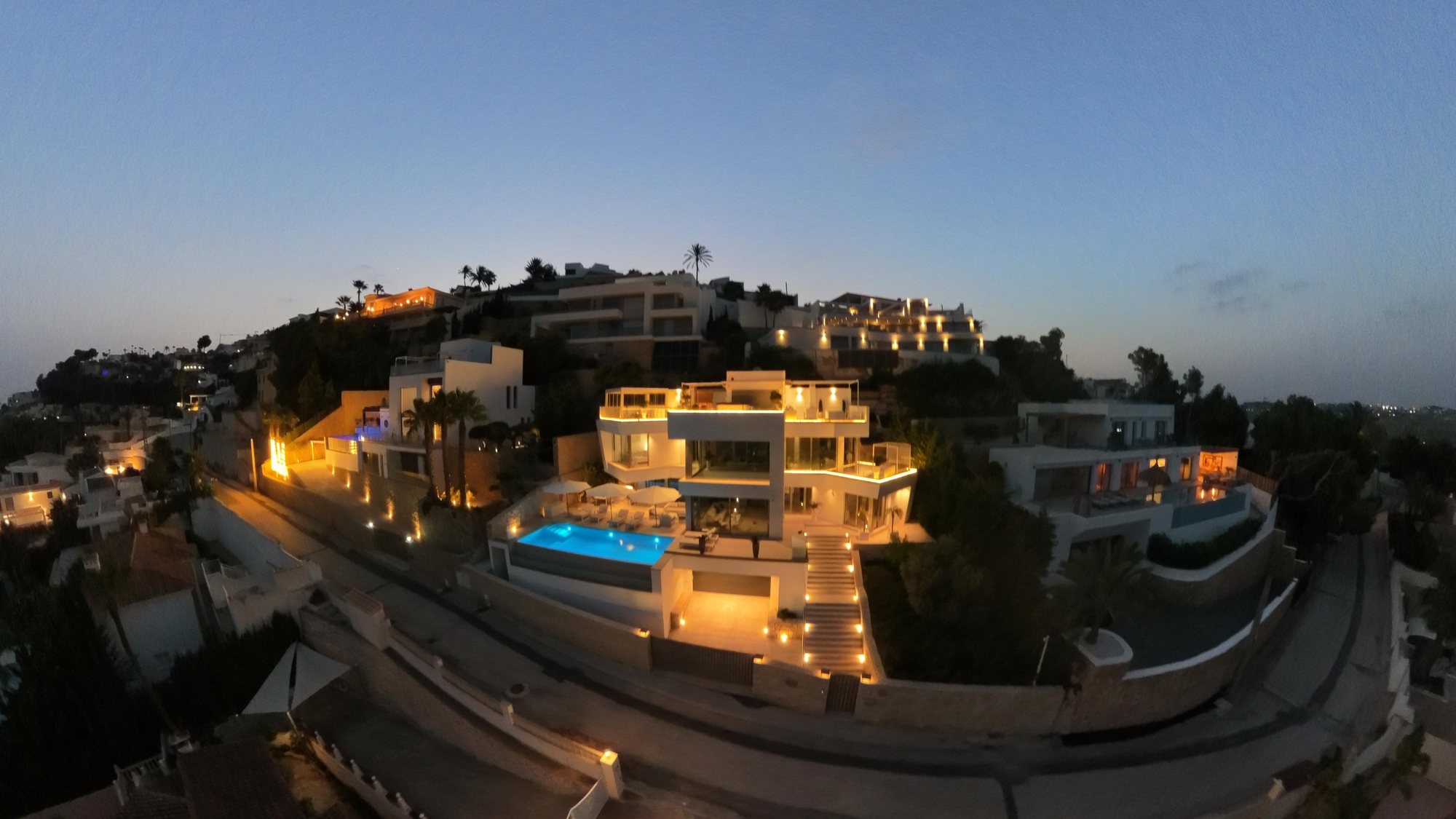 Die beleuchtete Villa Belia bei Nacht mit türkis leuchtendem Infinitypool